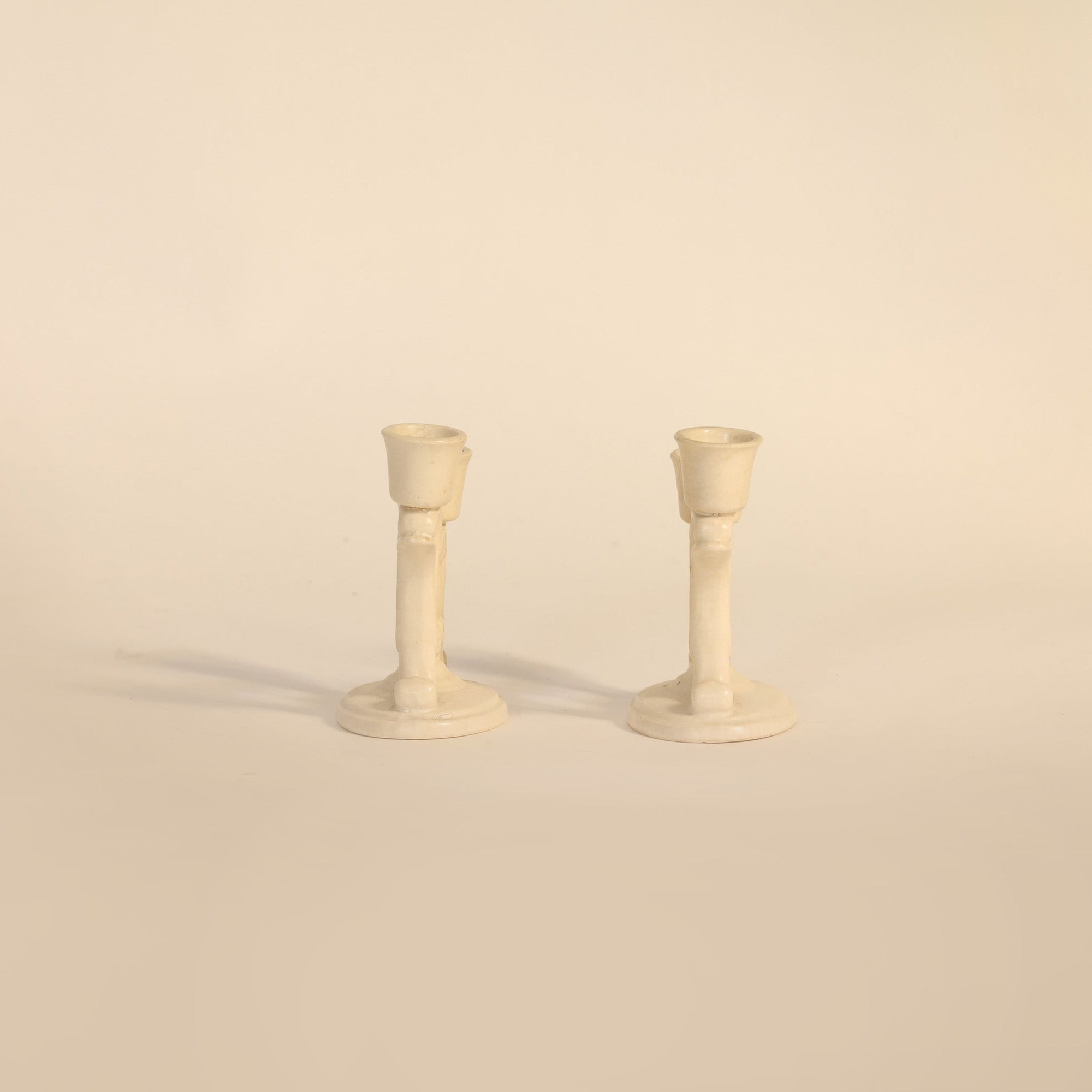 Two cream-colored candle holders on a beige background
