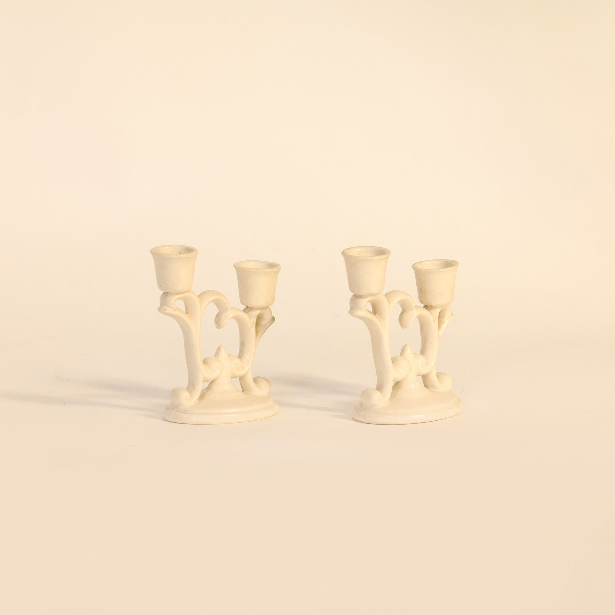 Two cream-colored candle holders on a beige background