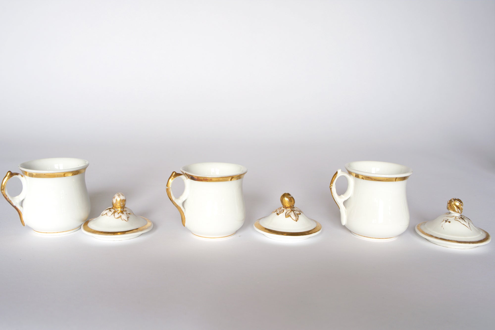 The Euro Trash Set of Breakfast Pots includes four white porcelain cups with gold trim and matching lids featuring gold finials, shown placed in front of each cup against a plain white background.