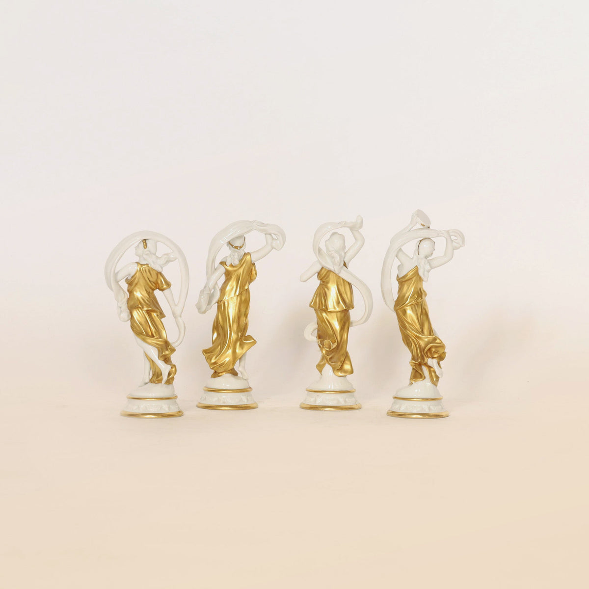 Set of Four Gilt & Porcelain Figurines by Euro Trash Annie, each depicting a woman in a flowing gold dress with graceful poses. Elegant gilt detailing accentuates the forms as the figurines transition from predominantly white on the left to richly gold on the right against a plain background.