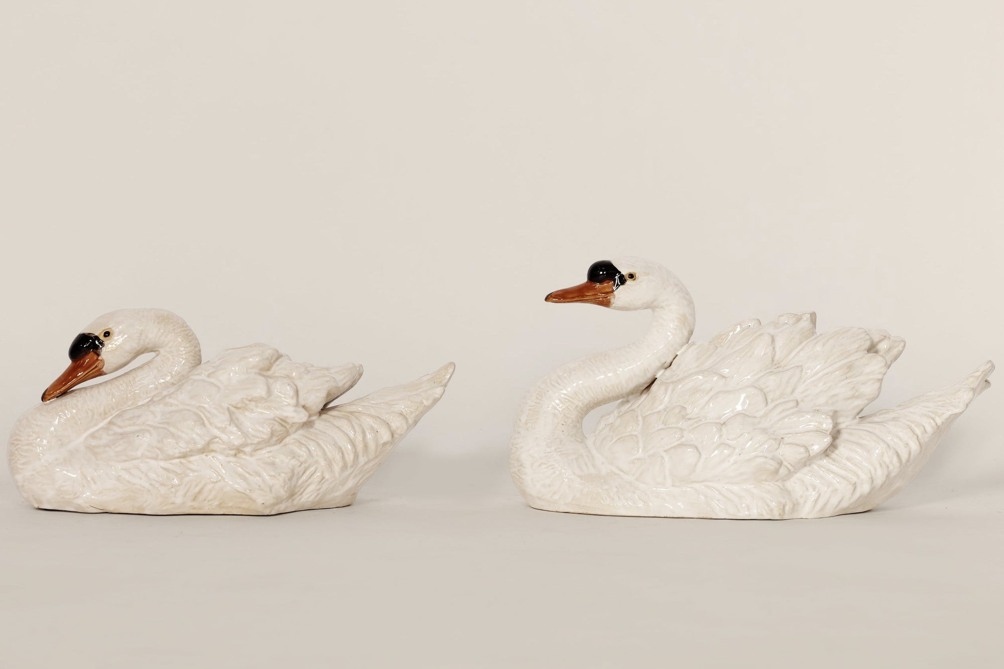 Two white ceramic swan figurines on a beige background