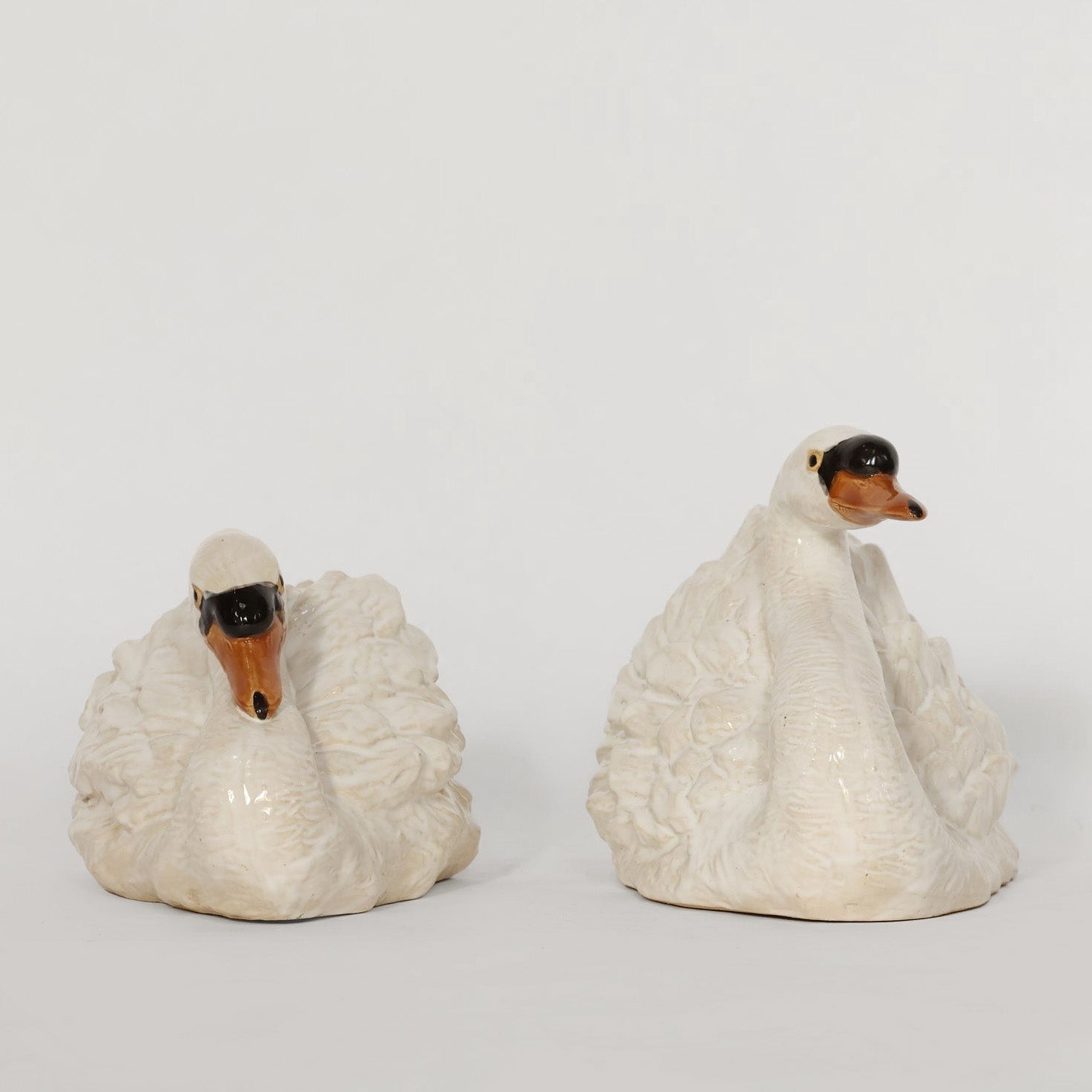 Two ceramic swan figures on a plain background