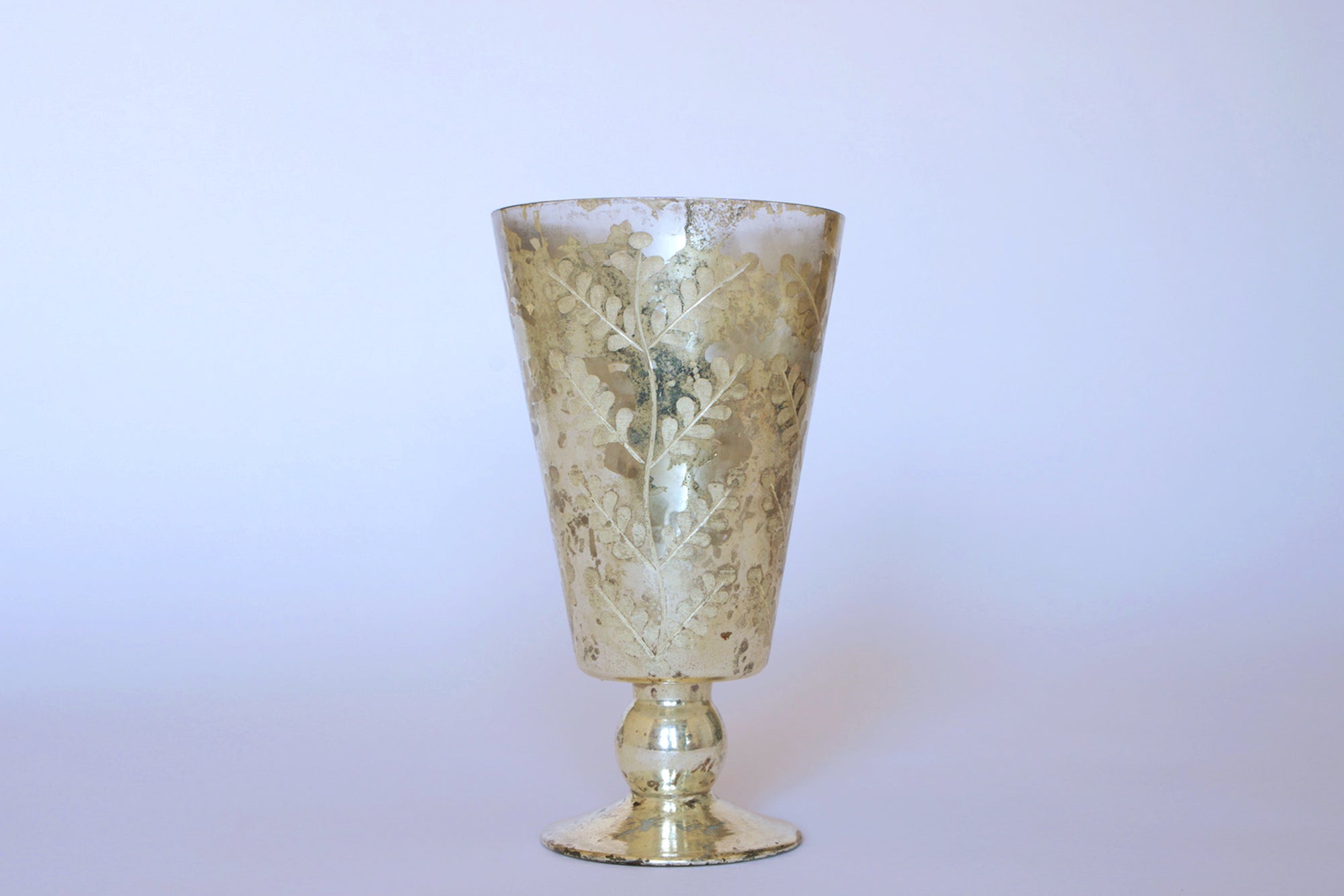 The Euro Trash Vintage Mercury Glass Vase features a silver finish with ornate etched leaf details, displayed against a plain light background.