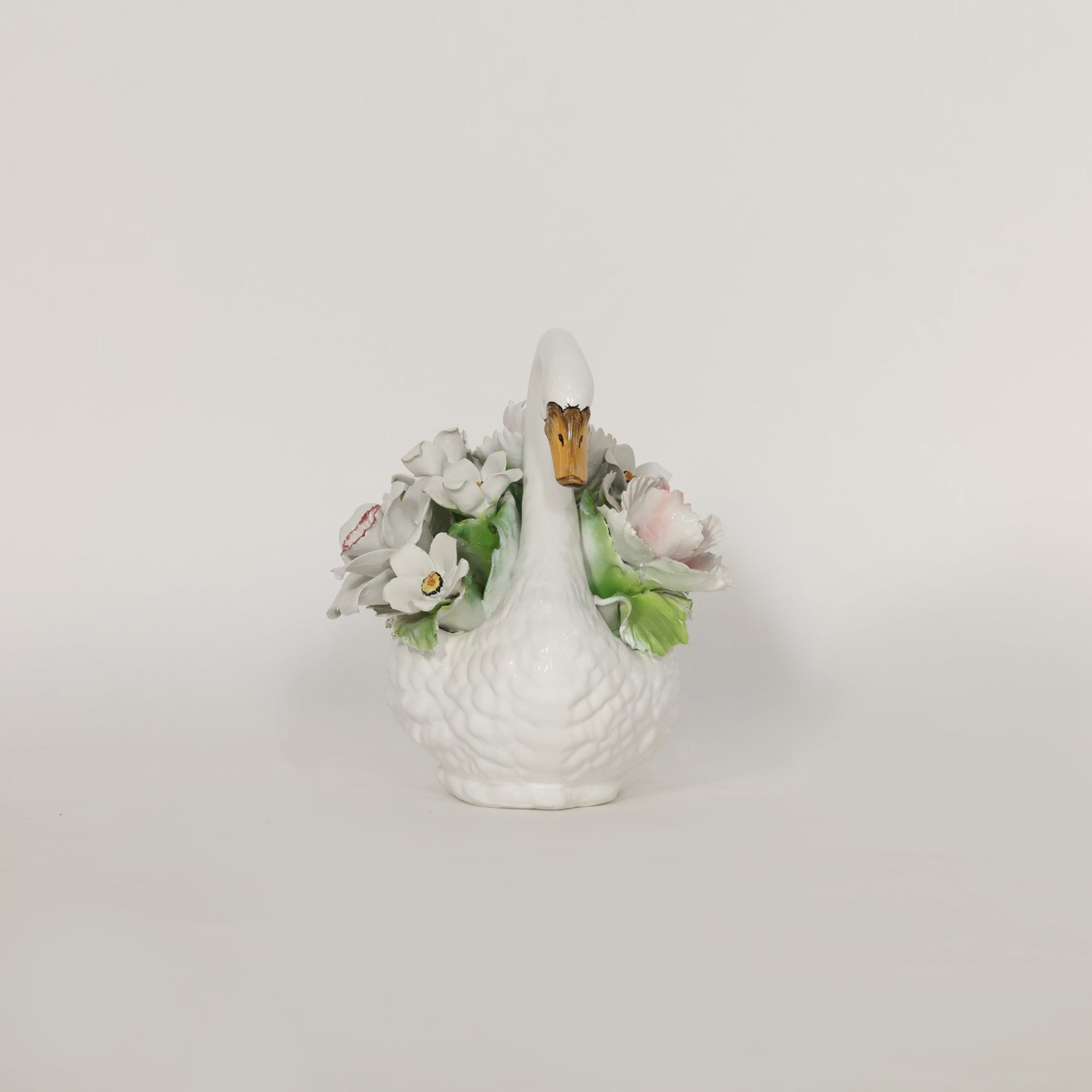 White ceramic swan figurine with floral decorations on a light gray background