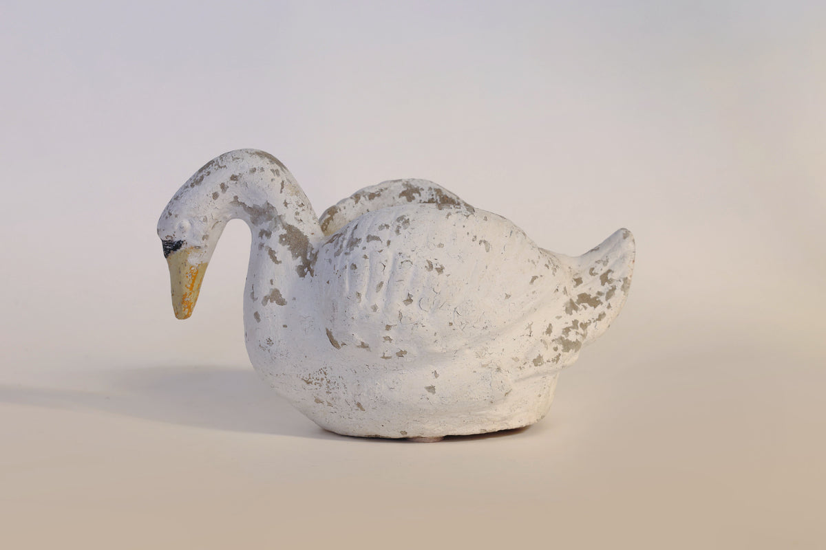 A Vintage Distressed Swan Planter by Euro Trash Annie, featuring a worn white ceramic finish with chipped paint, sits on a light surface against a neutral background, its sculptural form evoking classic vintage charm.