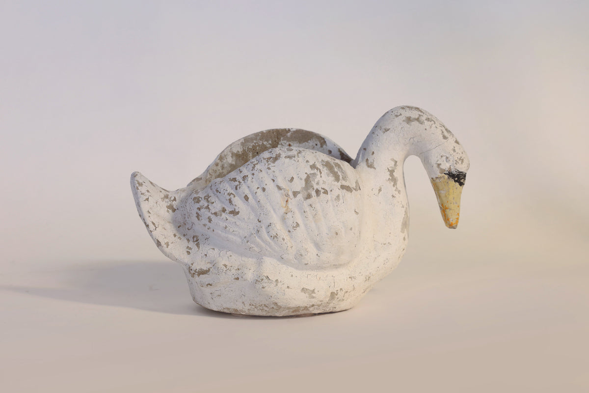 The Euro Trash Annie Vintage Distressed Swan Planter, featuring a weathered white ceramic finish with charming chipped paint, rests on a simple light surface, highlighting its unique vintage sculptural design.