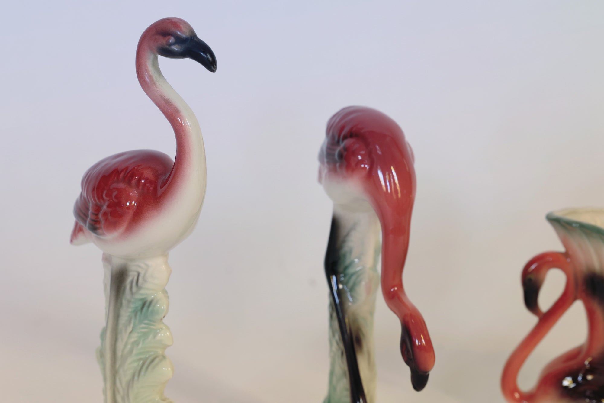The Euro Trash Annie Vintage Flamingo Figurines & Vase Set features three flamingo figurines—two standing upright and one with its head bent down—artfully painted in pink, white, and black hues, displayed against a simple light background for an elegant sculptural home decor accent.