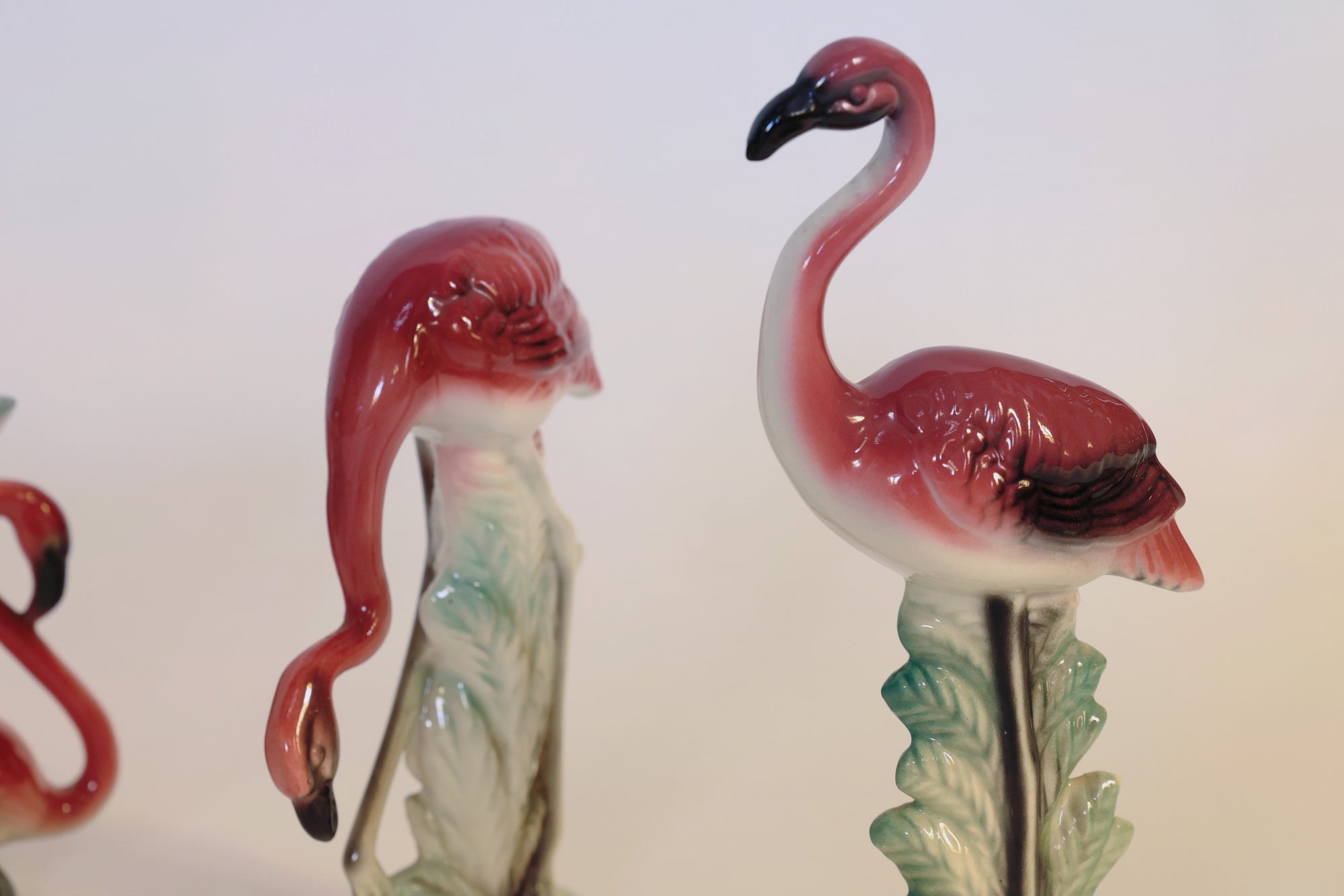 Add a touch of sculptural charm to your space with the Vintage Flamingo Figurines & Vase Set from Euro Trash Annie. This set features two glossy pink-and-white flamingos standing on green leafy bases—one with its head held high and the other gracefully curving its neck downward—making an eye-catching addition to your decor against a softly lit, plain background.