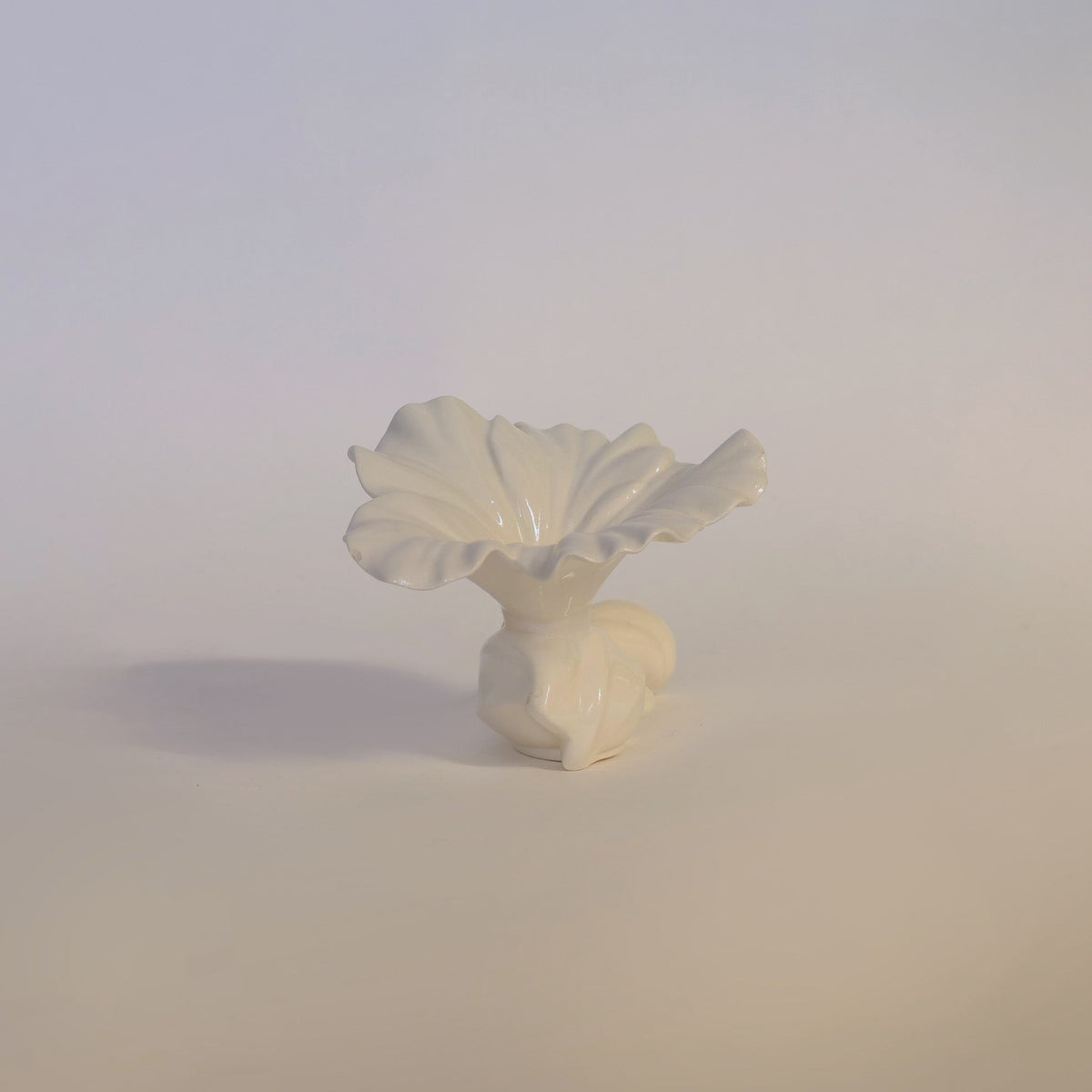 The Euro Trash Annie Vintage Milk Glass Ruffled Vase is a small, glossy white ceramic piece with an abstract flower shape and ruffled edge inspired by vintage milk glass, its opaque finish standing out beautifully against a soft, neutral background.