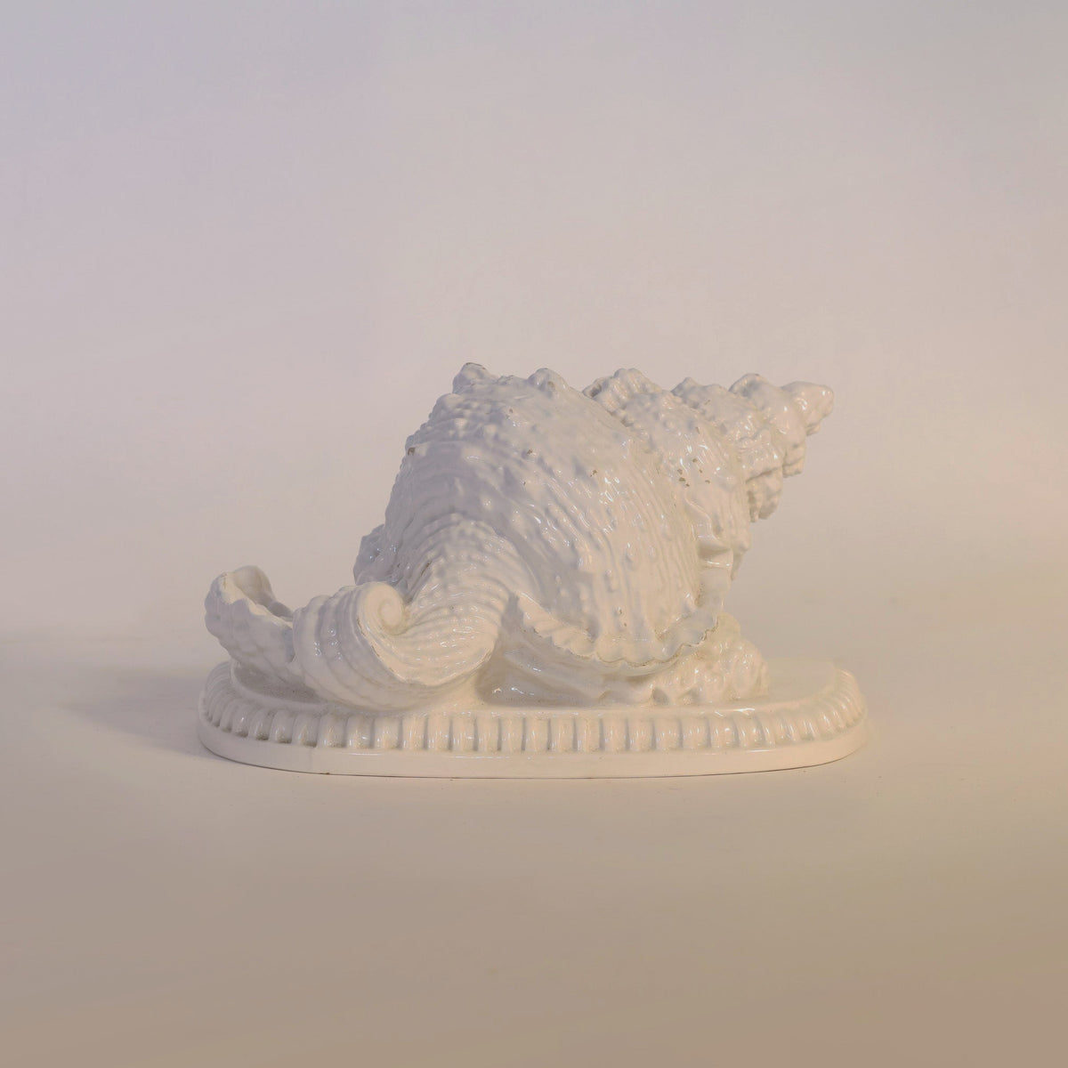 The Vintage Milk Glass Seashell Sculpture by Euro Trash Annie, crafted in white ceramic and set on an oval base, offers a refined touch of coastal decor against a plain light background, evoking the timeless charm of vintage seashell accents.