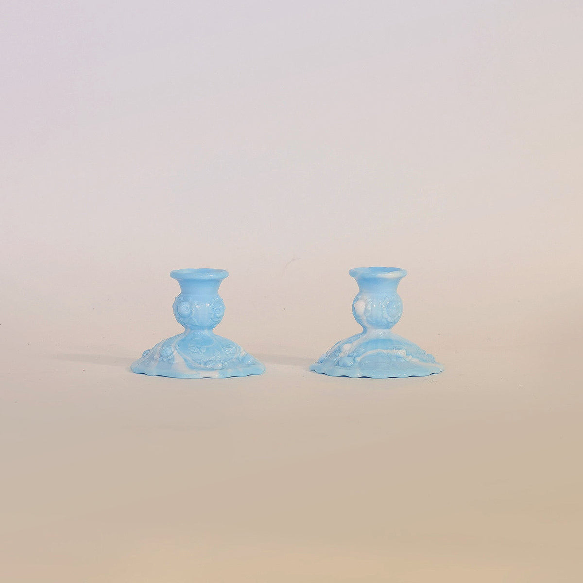 A Vintage Pair Of Blue Milk Glass Candlestick Holders by Euro Trash Annie are displayed side by side on a simple, light-colored surface with a neutral background.