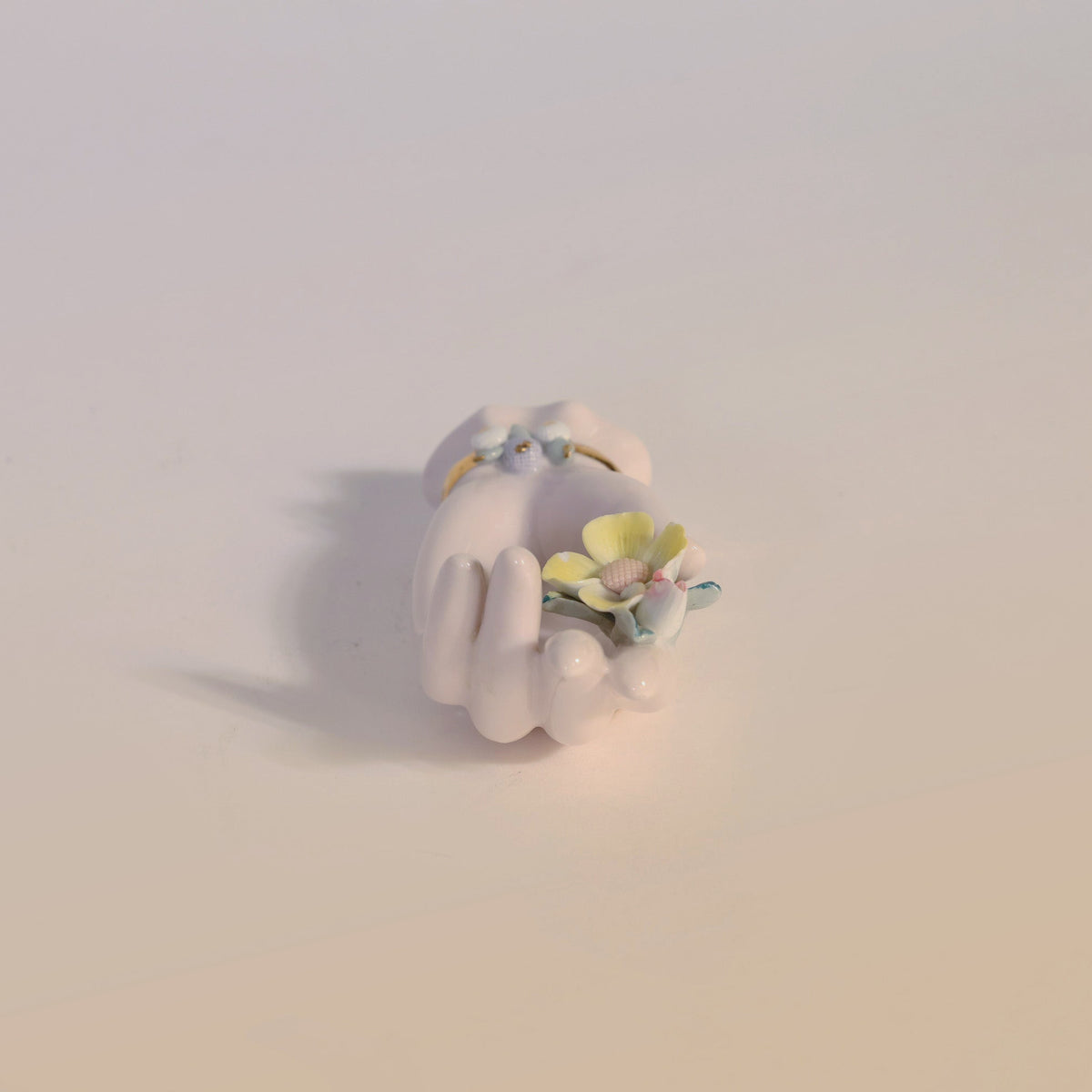 The Euro Trash Annie Vintage Porcelain Hand Ring Holder in a small white design gracefully displays delicate pastel-colored flowers, resting on a softly shaded surface as a charming decorative accent.