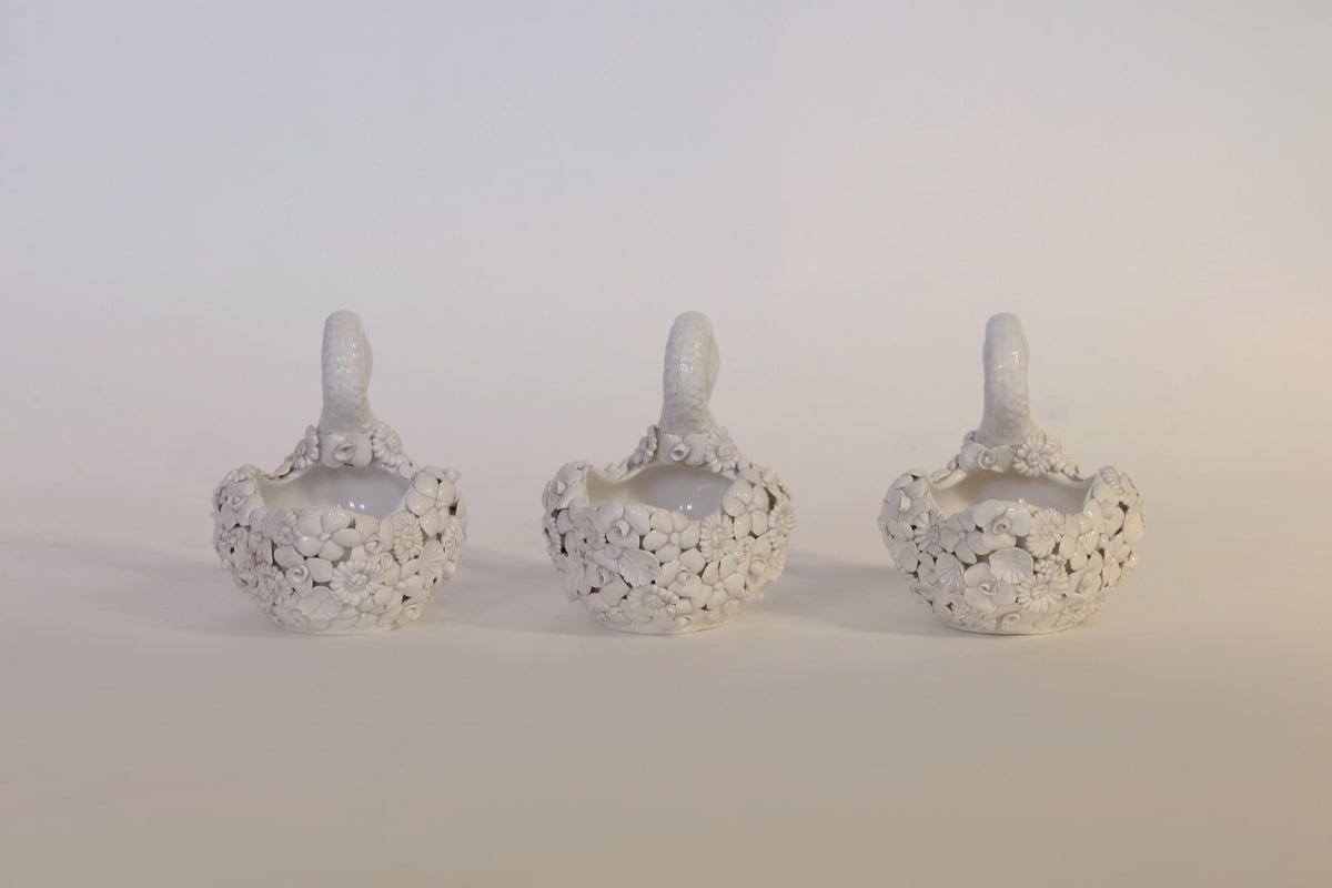 Three small, white ceramic swan planters with textured floral detailing and handles from Euro Trash Annie’s Vintage Set Of Floral Swan Planters are arranged side by side on a plain, light background. These charming pieces serve as lovely decorative accents for any space.