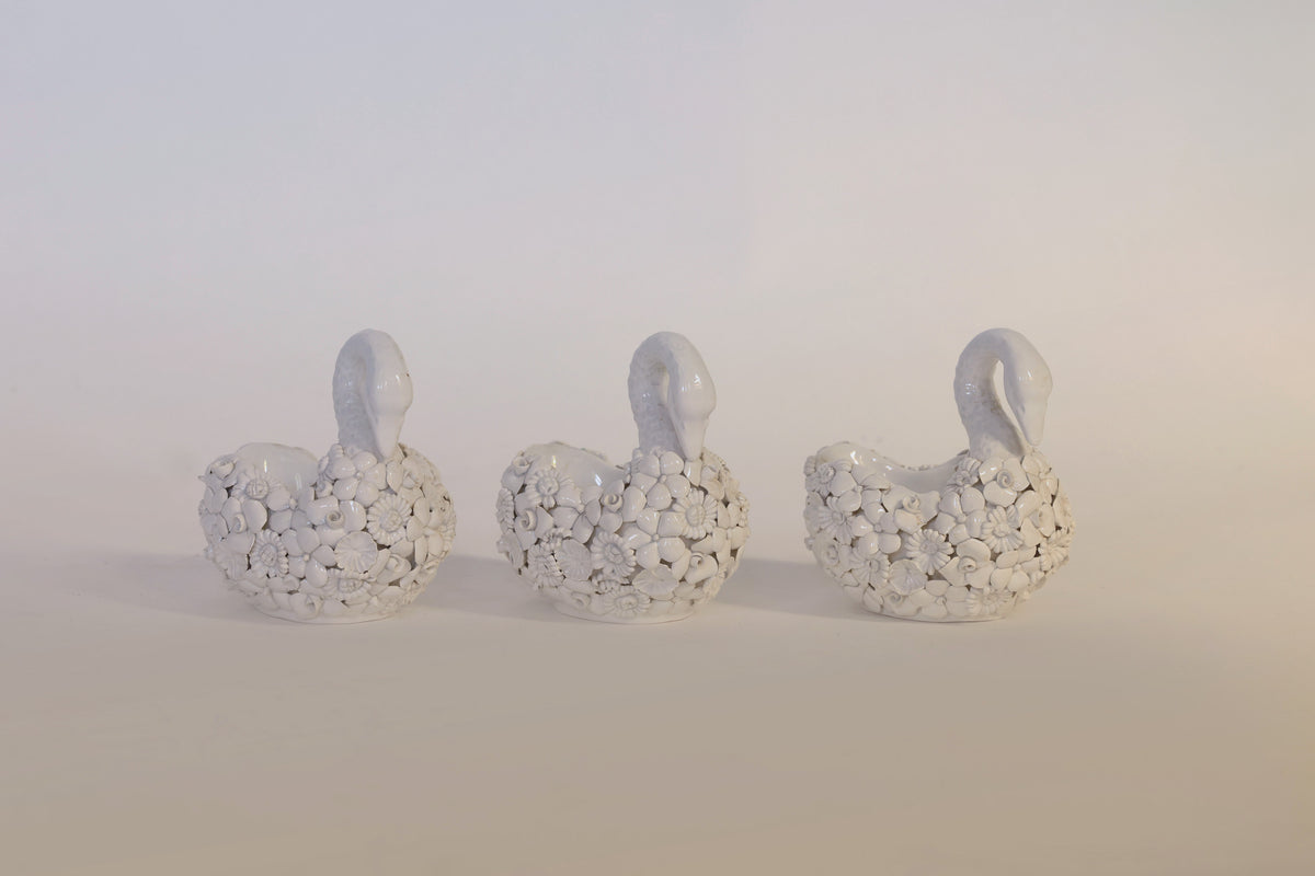 A set of three white ceramic swan planters by Euro Trash Annie, featuring vintage-inspired floral patterns and textured detailing, are arranged in a row against a light background, making charming decorative accents with their intricate design.