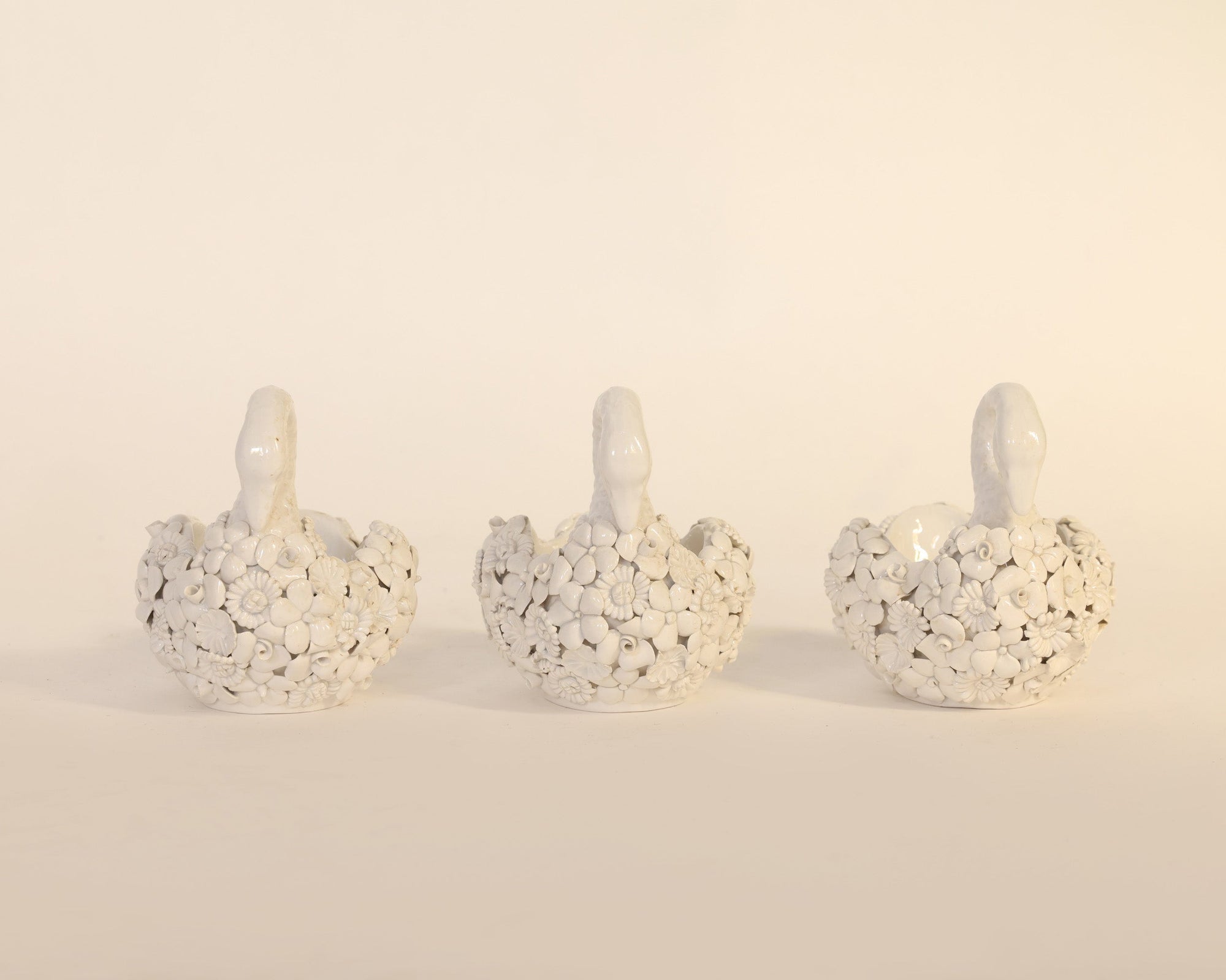 Three decorative swan figurines with a textured surface on a beige background