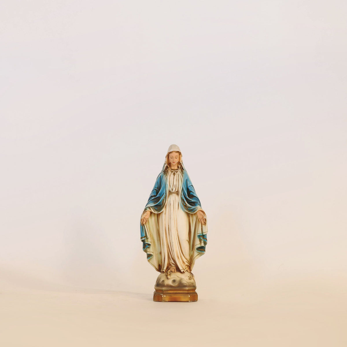 This Vintage Virgin Mary Statue by Euro Trash Annie features serene blue and white robes and stands gracefully on a small pedestal against a plain, light background, making it an ideal piece for spiritual home decor.
