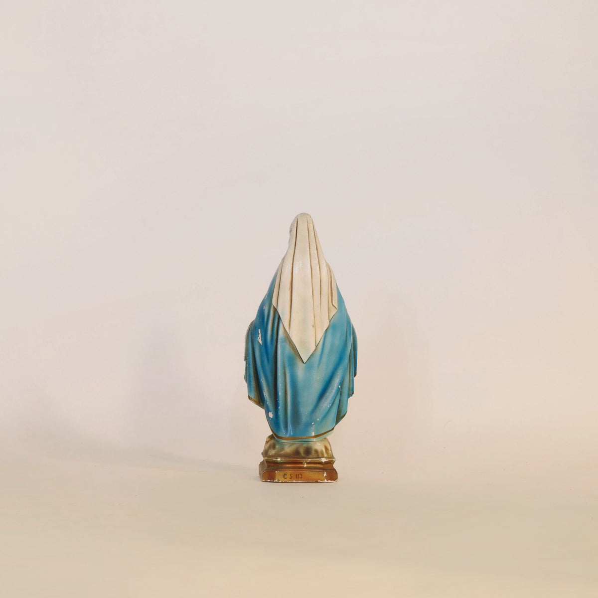 The Euro Trash Annie Vintage Virgin Mary Statue features a serene, robed figure draped in blue and white, elegantly viewed from behind as she stands on a small pedestal against a plain light background. Ideal as spiritual home decor, this piece exudes tranquility and devotion.