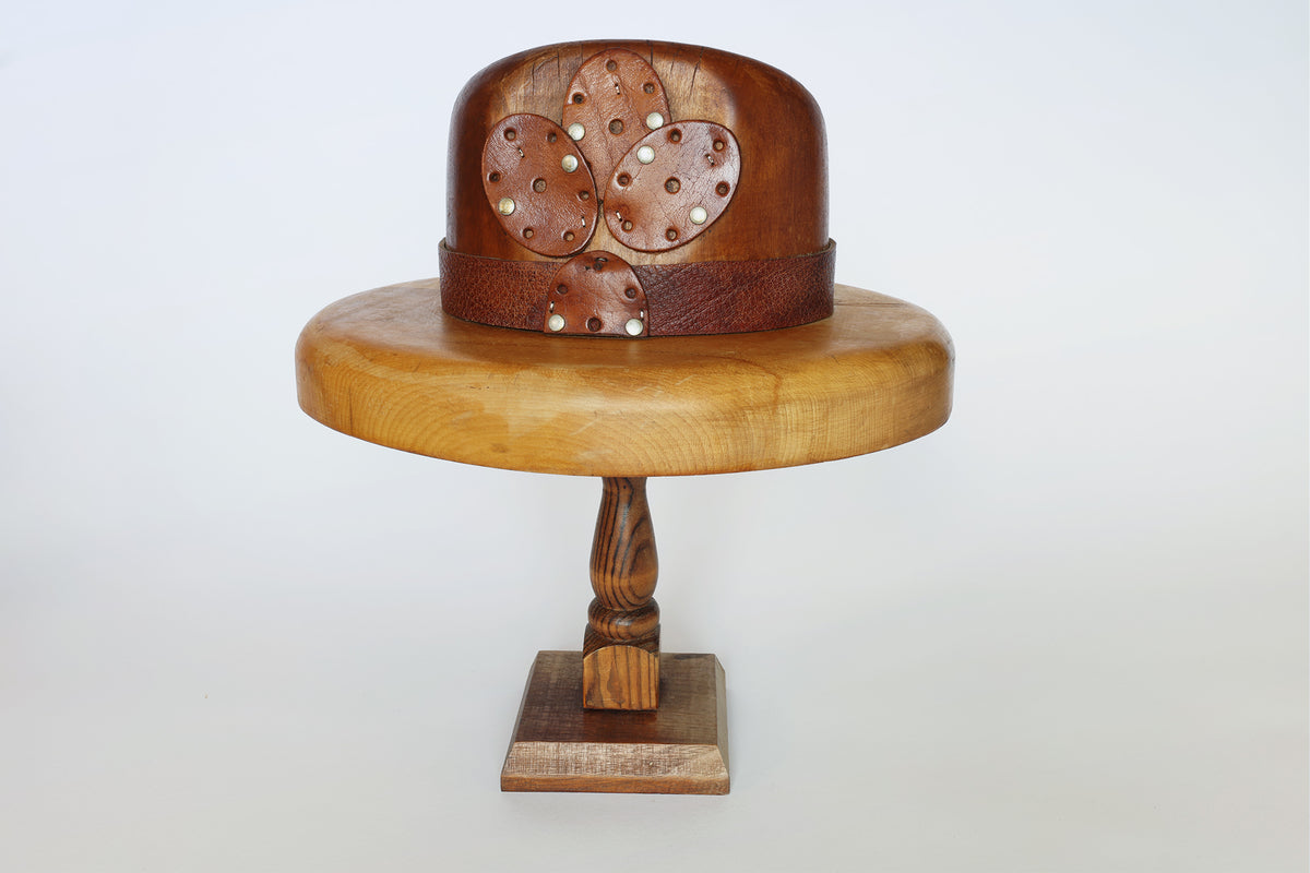 A Vintage Wooden Millinery Hat Mold by Euro Trash is displayed against a plain white background, featuring a wide-brimmed wooden hat adorned with oval-shaped perforated wooden accents and a textured band, all set on a vintage hat mold stand.
