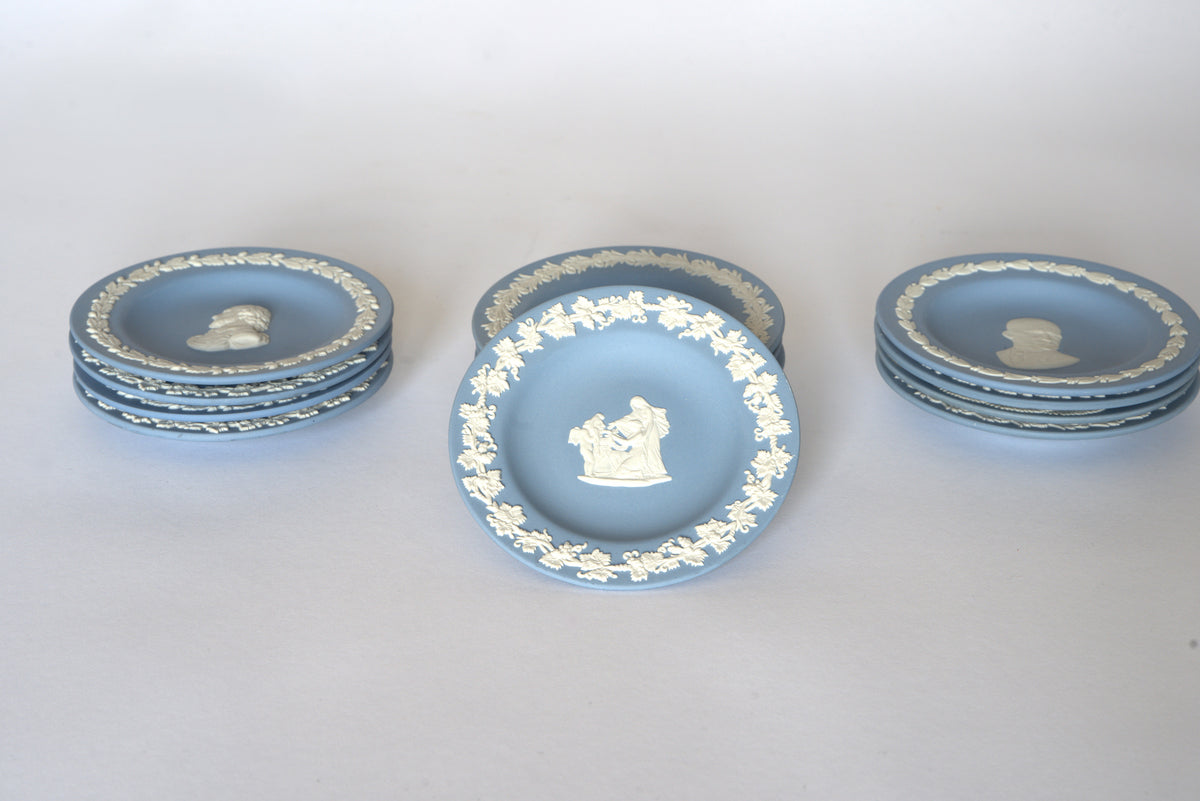 Euro Trash Vintage Blue Jasperware Style Relief Plates: six blue plates with white neoclassical designs—four stacked left, three right, plus one central decorative plate featuring a white relief of figures.