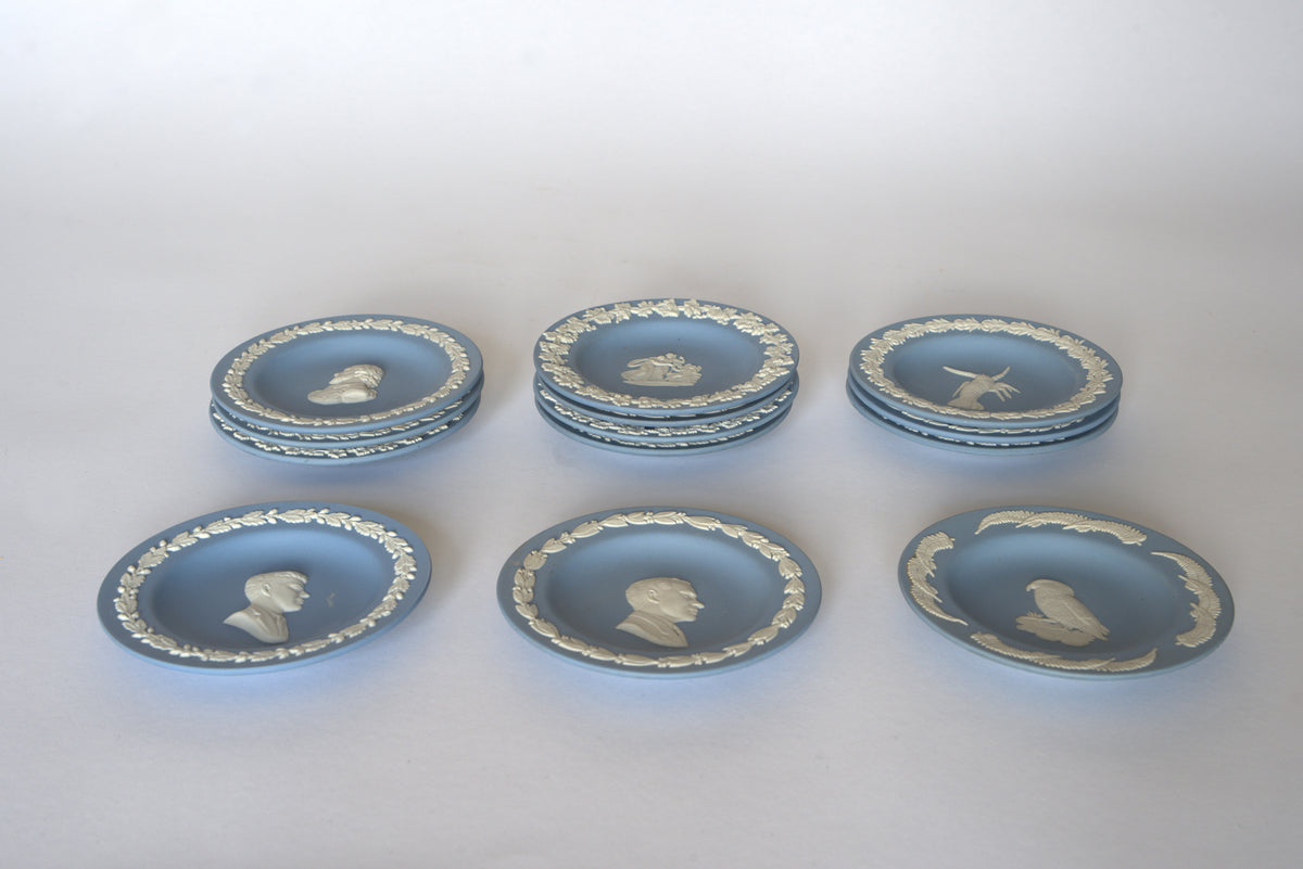 Seven Euro Trash Vintage Blue Jasperware Style Relief Plates, adorned with profiles, animals, and floral motifs, are arranged in three rows on a light background to form an elegant decorative wall display set.