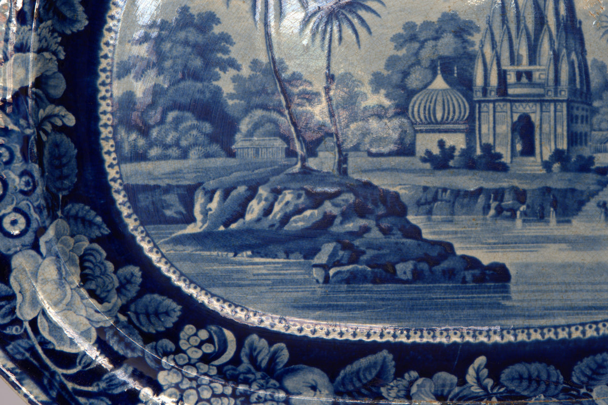 The Vintage Blue & White Floral Transferware Serving Platter by Euro Trash features floral rim patterns and a scenic design with palm trees, rocks, and ornate domed buildings.