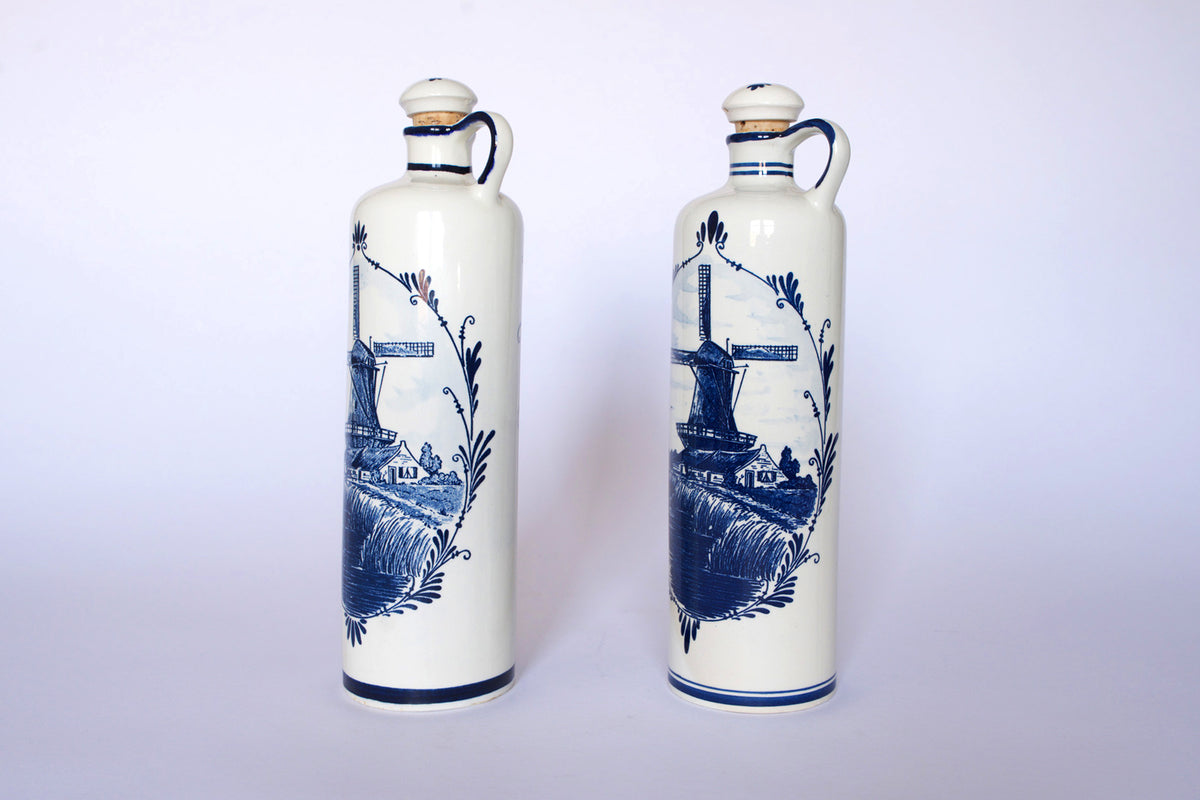 The Euro Trash Vintage Blue & White Windmill Motif Ceramic Bottle Decanters feature two tall, handled bottles with cork stoppers and classic windmill designs, set against a plain white background.