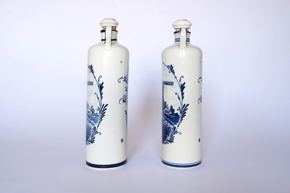 The Euro Trash Vintage Blue & White Windmill Motif Ceramic Bottle Decanters feature tall ceramic bottles with scenic windmill designs, displayed upright on a plain white background as a charming decorative set.