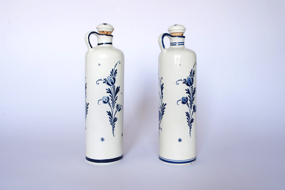 Euro Trash Vintage Blue & White Windmill Motif Ceramic Bottle Decanters—two tall bottles with handles, cork and ceramic stoppers—stand side by side as a charming decorative set against a plain white background.