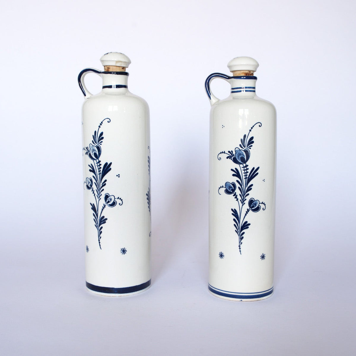 Two Euro Trash Vintage Blue & White Windmill Motif Ceramic Bottle Decanters, each with a handle and cork stopper, stand side by side on a plain white background.