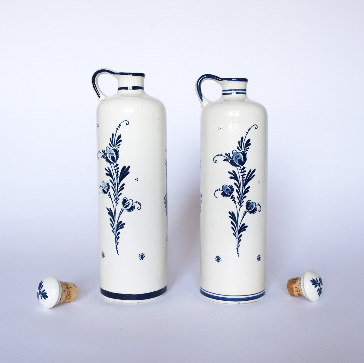 The Euro Trash Vintage Blue & White Windmill Motif Ceramic Bottle Decanters feature tall ceramic bottles with handles, matching cork stoppers, and classic blue windmill designs, making a charming decorative set against a plain white background.