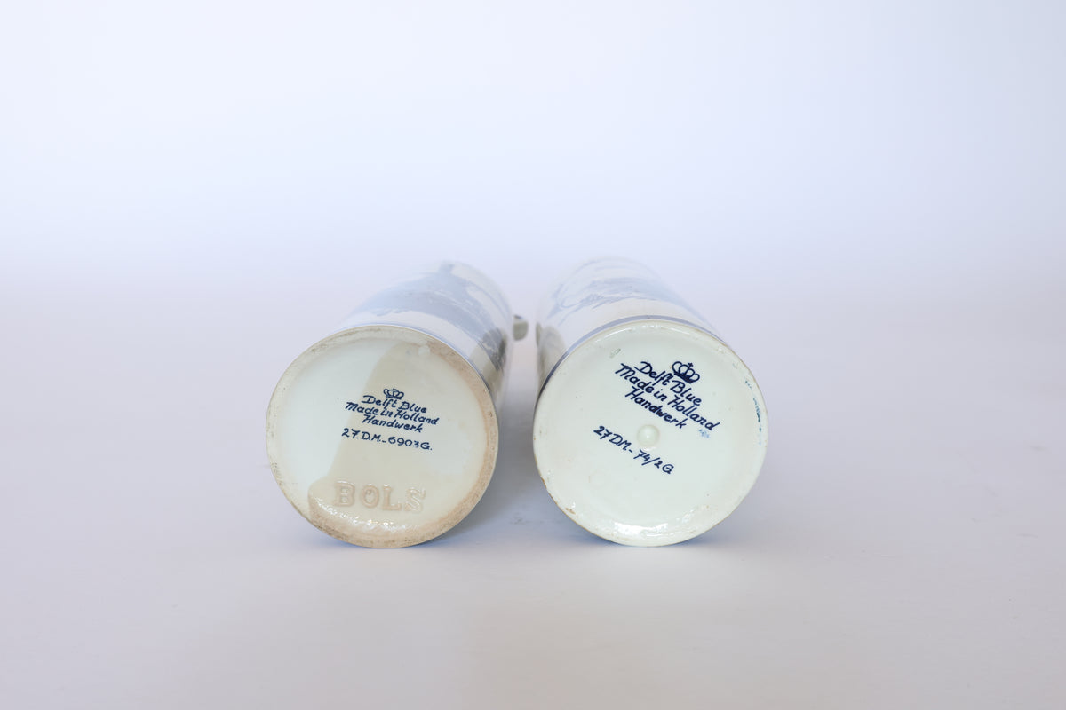 Two Vintage Blue & White Windmill Motif Ceramic Bottle Decanters by Euro Trash are shown lying on their sides, bases with blue branding visible, including one marked "BOLS," all against a plain white background.