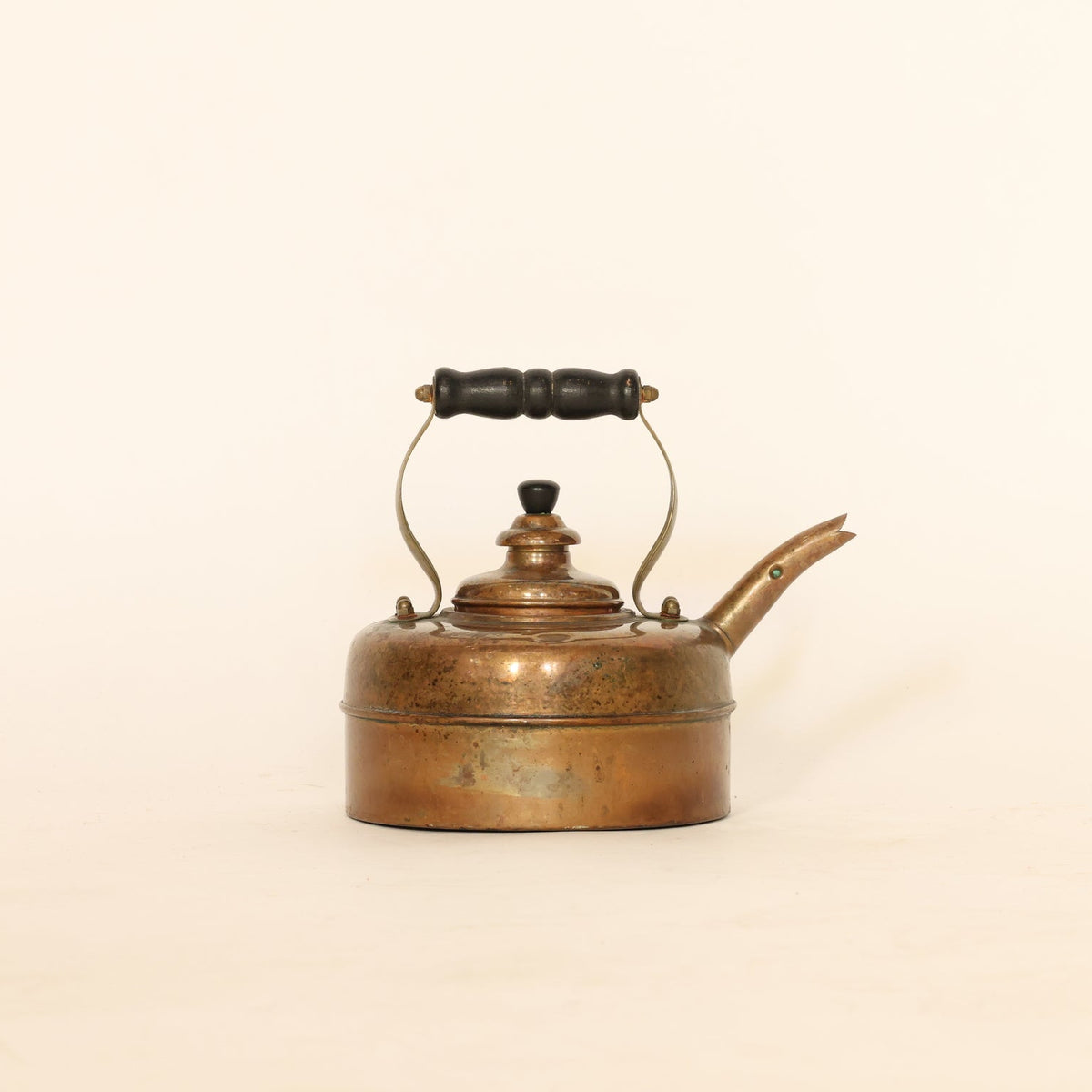 Vintage copper kettle with a black handle on a beige background