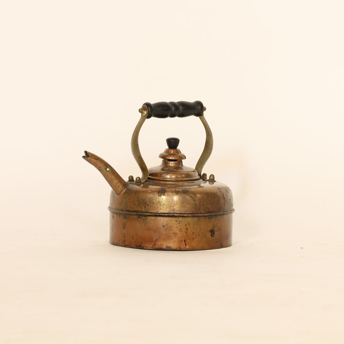 Vintage copper kettle with a black handle on a beige background