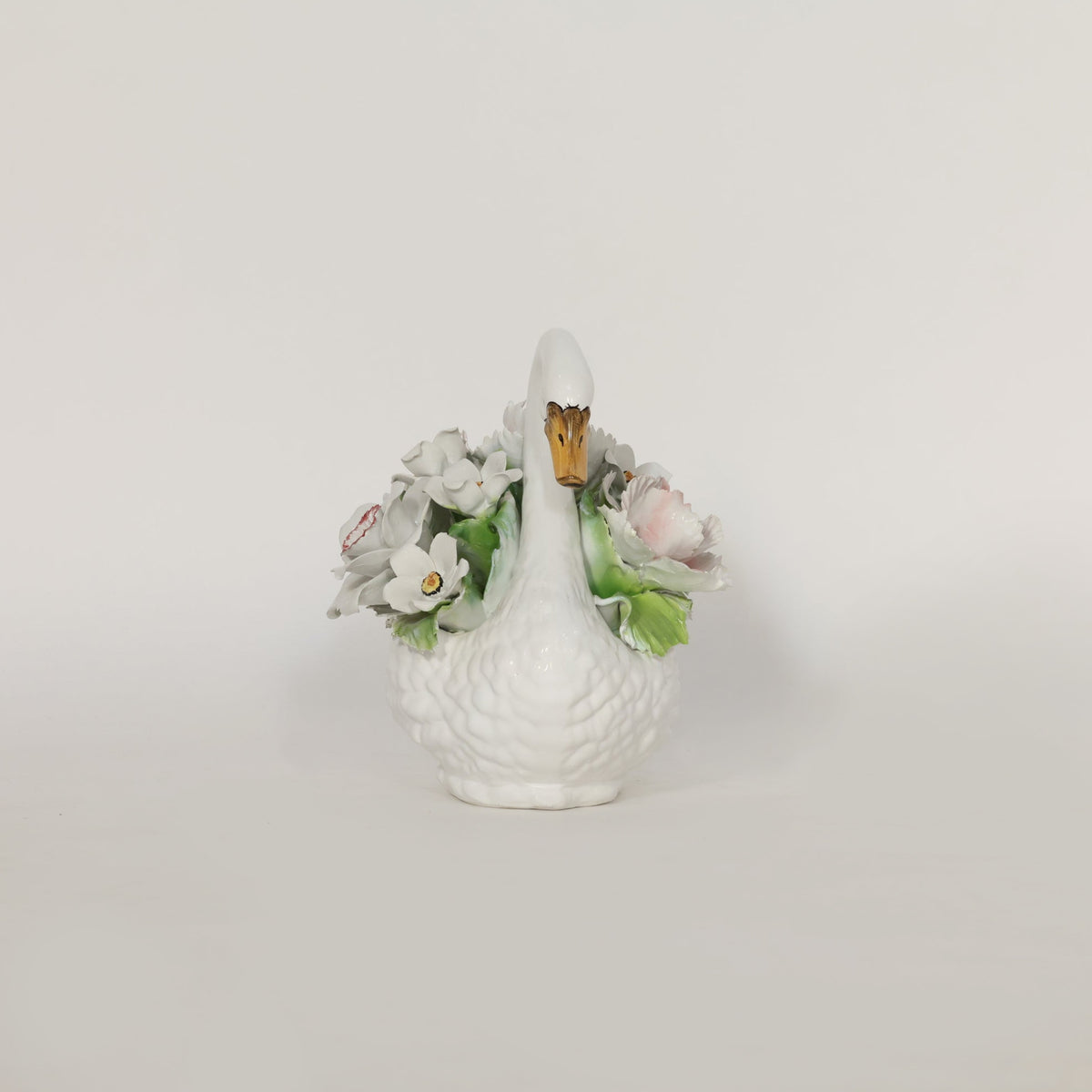 White ceramic swan figurine with floral decorations on a light gray background