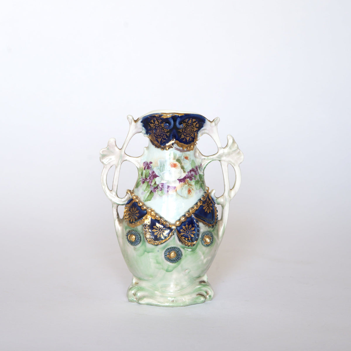 Euro Trash Vintage Hand-Painted Floral Porcelain Vase with cobalt and gold accents, featuring two handles and adorned with roses and intricate blue and gold floral designs on a white and green background, showcased against a plain white backdrop.