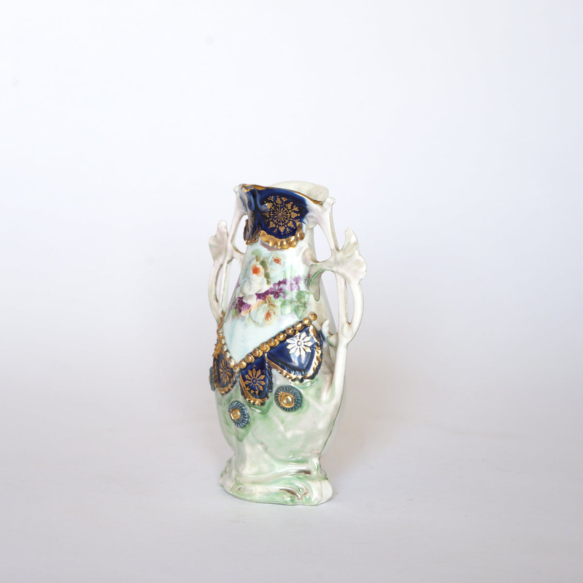 Euro Trash Vintage Hand-Painted Floral Porcelain Vase with Cobalt and Gold Accents, featuring ornate blue and gold detailing, sculpted handles, hand-painted roses, and intricate floral patterns, displayed against a plain white background.