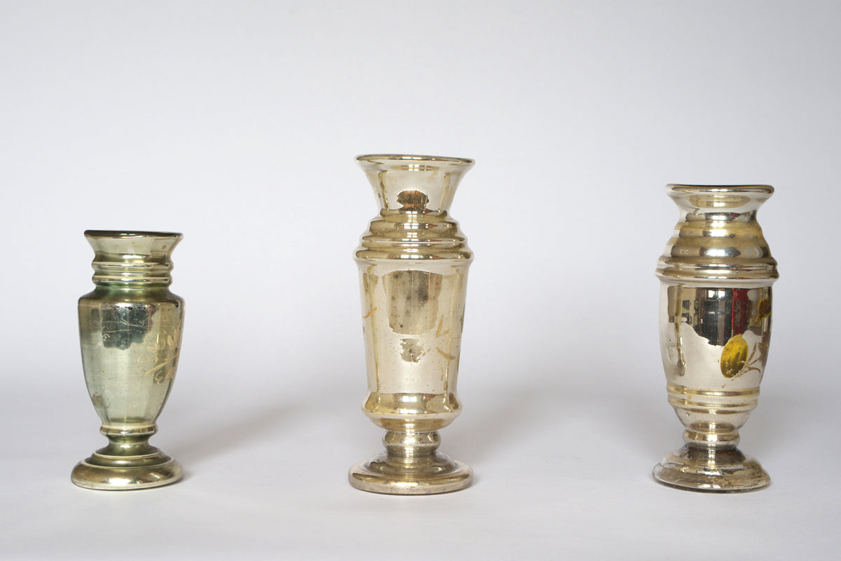 The Euro Trash Vintage Hand-Painted Mercury Glass Vase Set includes three vases of different shapes and heights, each with a reflective, gently tarnished finish for timeless appeal, displayed against a plain white background.