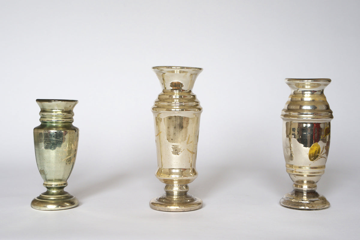 The Euro Trash Vintage Hand-Painted Mercury Glass Vase Set features three uniquely shaped vases with reflective, silvered finishes and charming tarnish detail, creating an elegant, antique display against a plain white background.