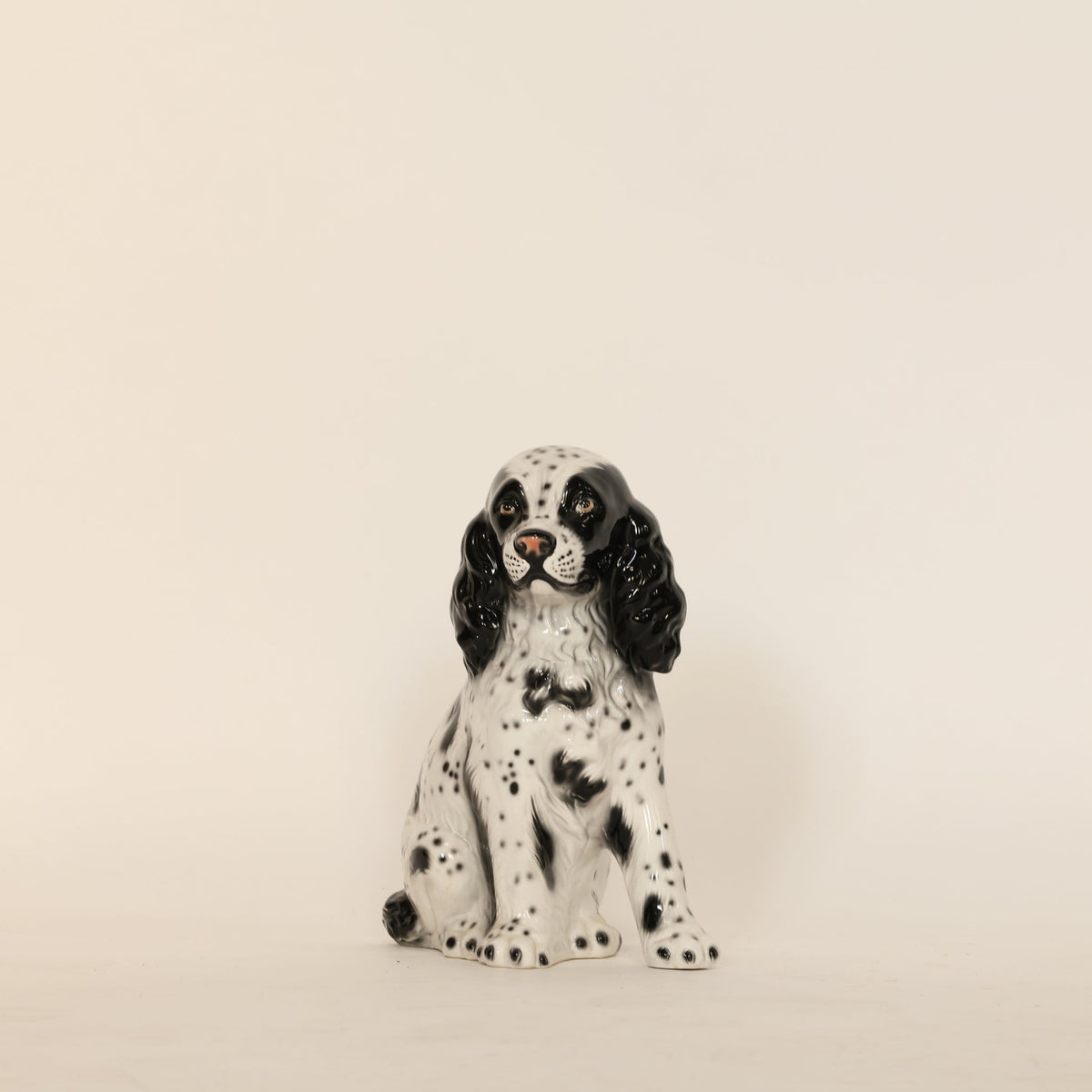 Ceramic dog figurine with black and white spots on a beige background