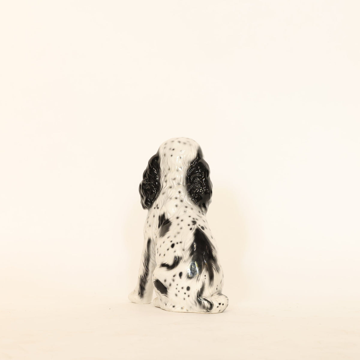 Small ceramic dog figurine with black spots on a beige background