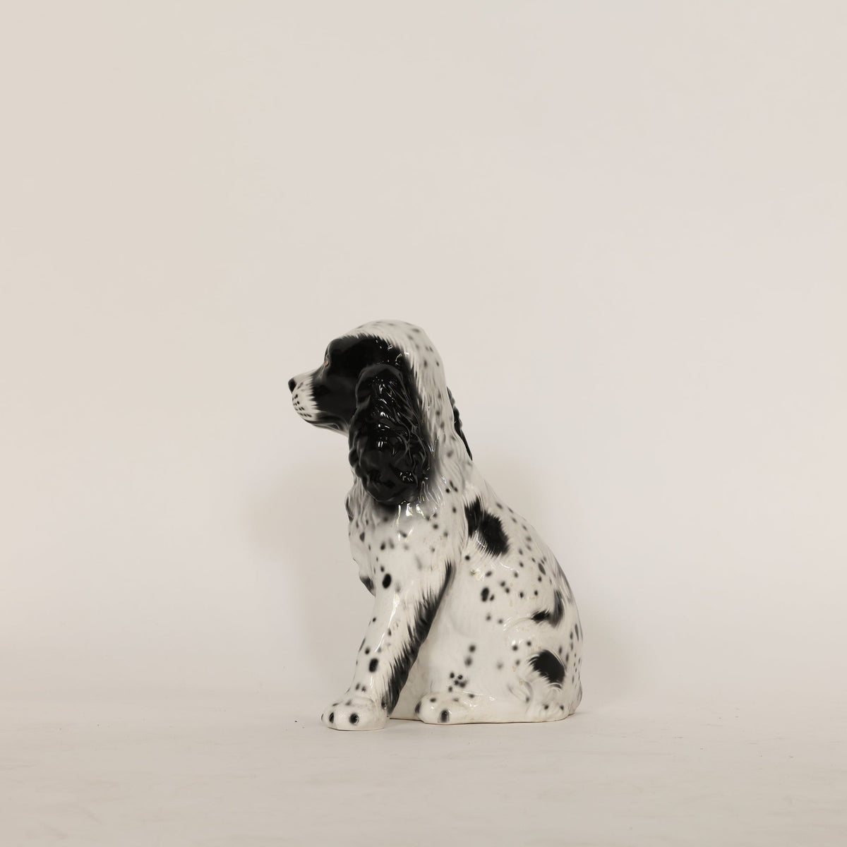 Ceramic dog figurine with black spots on a beige background