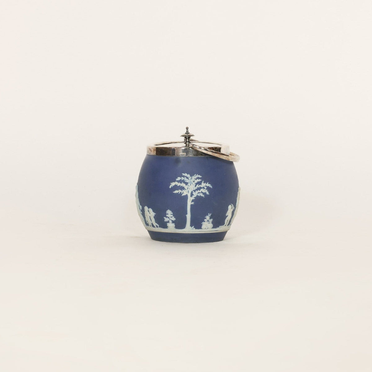 Decorative blue and white ceramic jar with silver lid on a light beige background