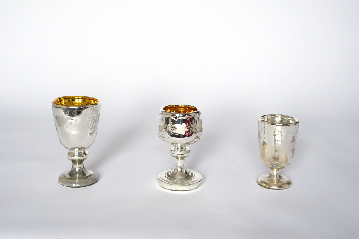The Euro Trash Vintage Mercury Glass Stemmed Cup Set features three uniquely shaped cups with gold interiors and etched details, displayed side by side on a white background—an ideal decorative accent for any collection.