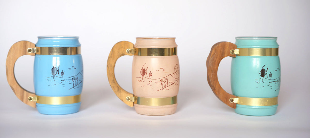 The Euro Trash Vintage Pastel Glass Mug Set includes three mugs in blue, beige, and turquoise, each featuring a hand-drawn coastal scene—stylish for tiki drinks and perfect for enhancing your mid-century barware collection.