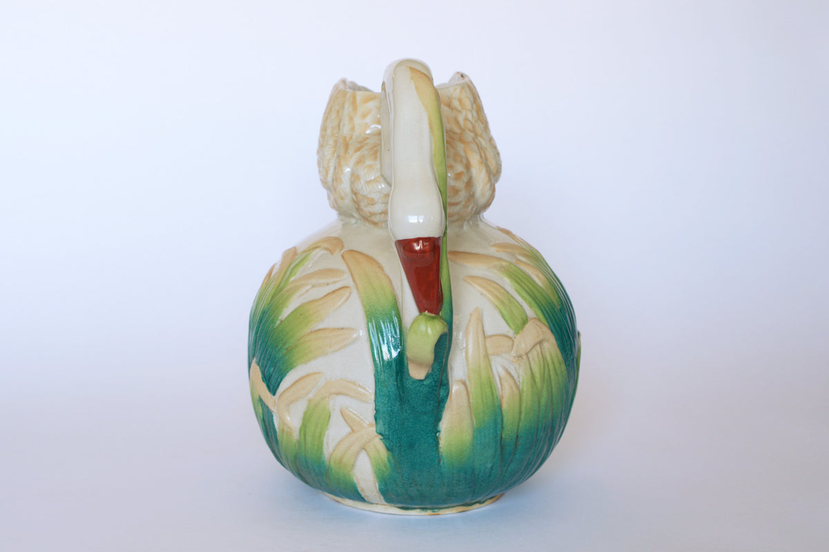 The Euro Trash Vintage Swan Motif Ceramic Pitcher features a hand-painted swan design with a beige body, red-tipped beak, and cattail accents in green and yellow, shown against a plain white background.