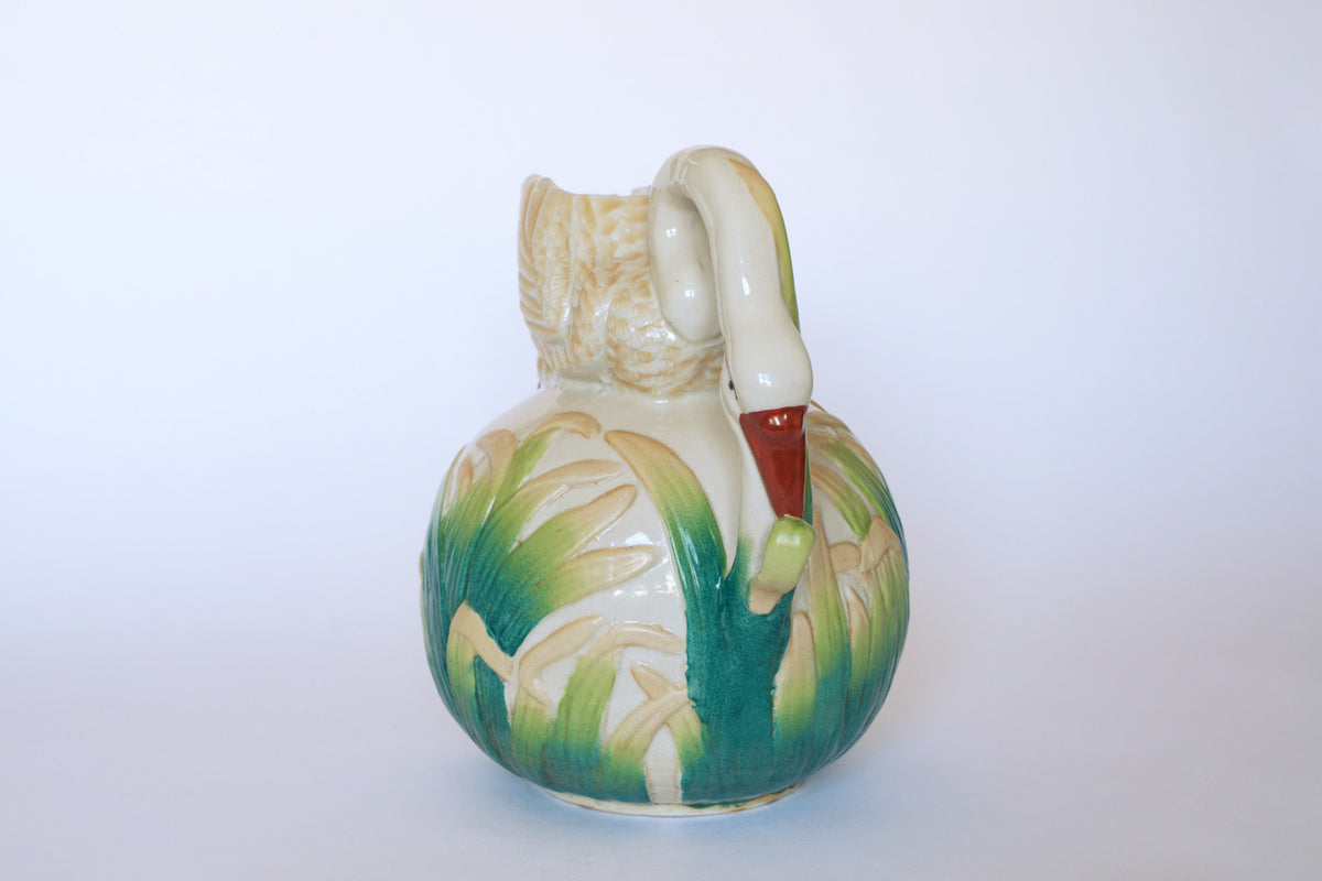 The Euro Trash Vintage Swan Motif Ceramic Pitcher features a swan-shaped handle and hand-painted green and yellow cattail designs, all set on a pure white background.