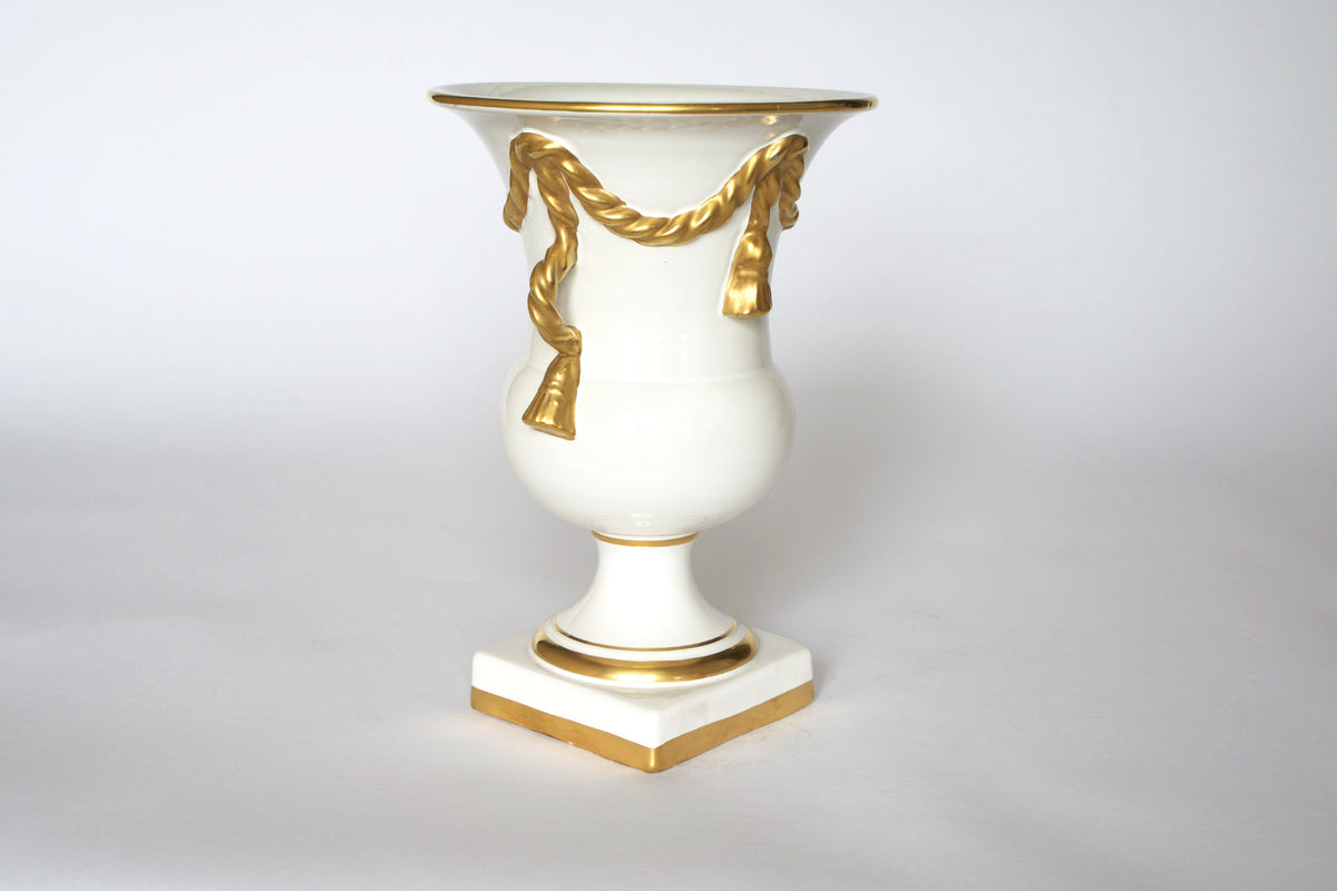 The Euro Trash Vintage White & Gold Urn Vase with Draped Garland Detail features a neoclassical flared rim, elegant gold accents, and stands on a square base—a timeless decorative piece against a white background.