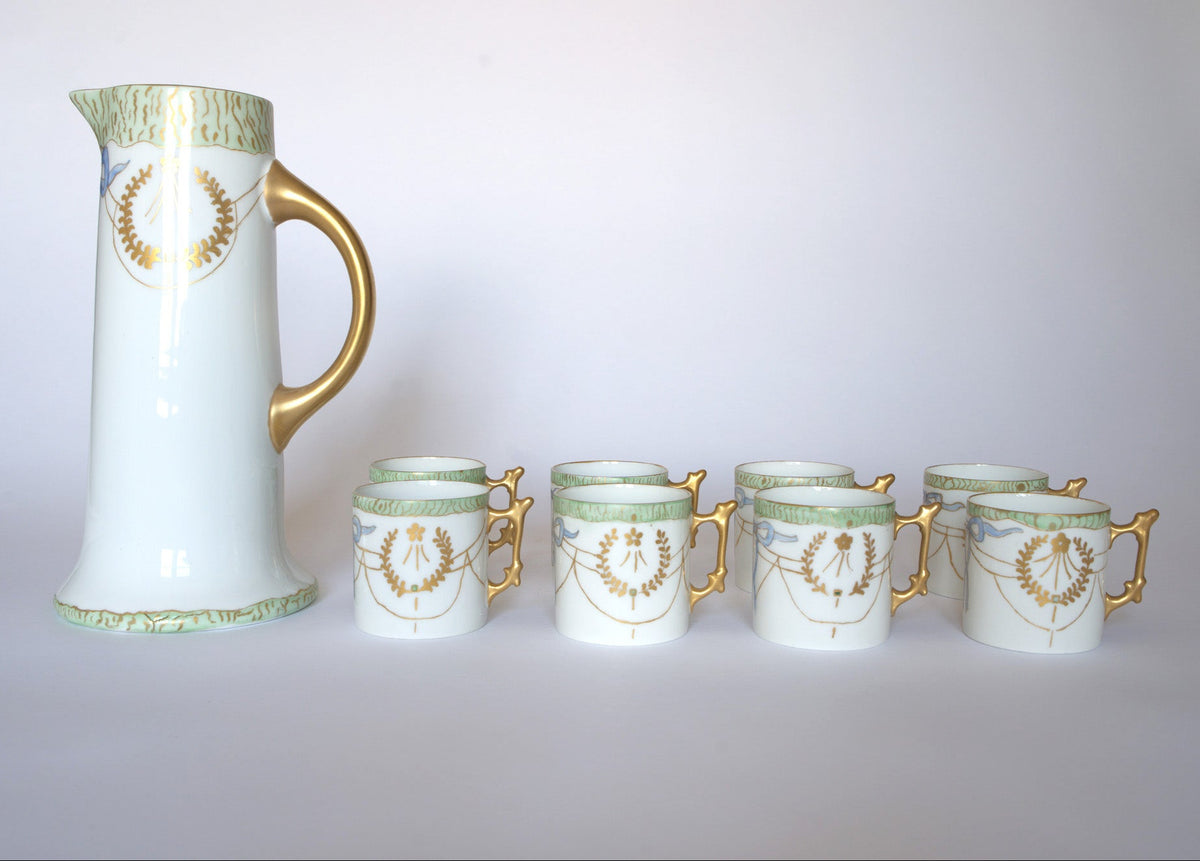 The Euro Trash Vintage White Porcelain Teacup Set with Gold Handle features a classic white pitcher and five matching cups, each with gold handles and elegant green and gold patterns, artistically displayed on a light background.