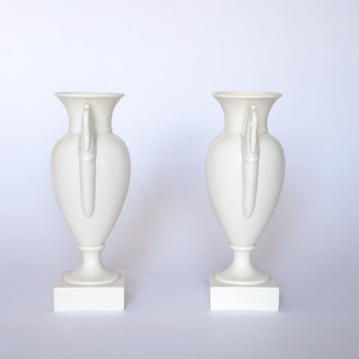 A pair of Vintage White Swan Handle Ceramic Urn Vases by Euro Trash stand side by side on square bases against a plain white background.