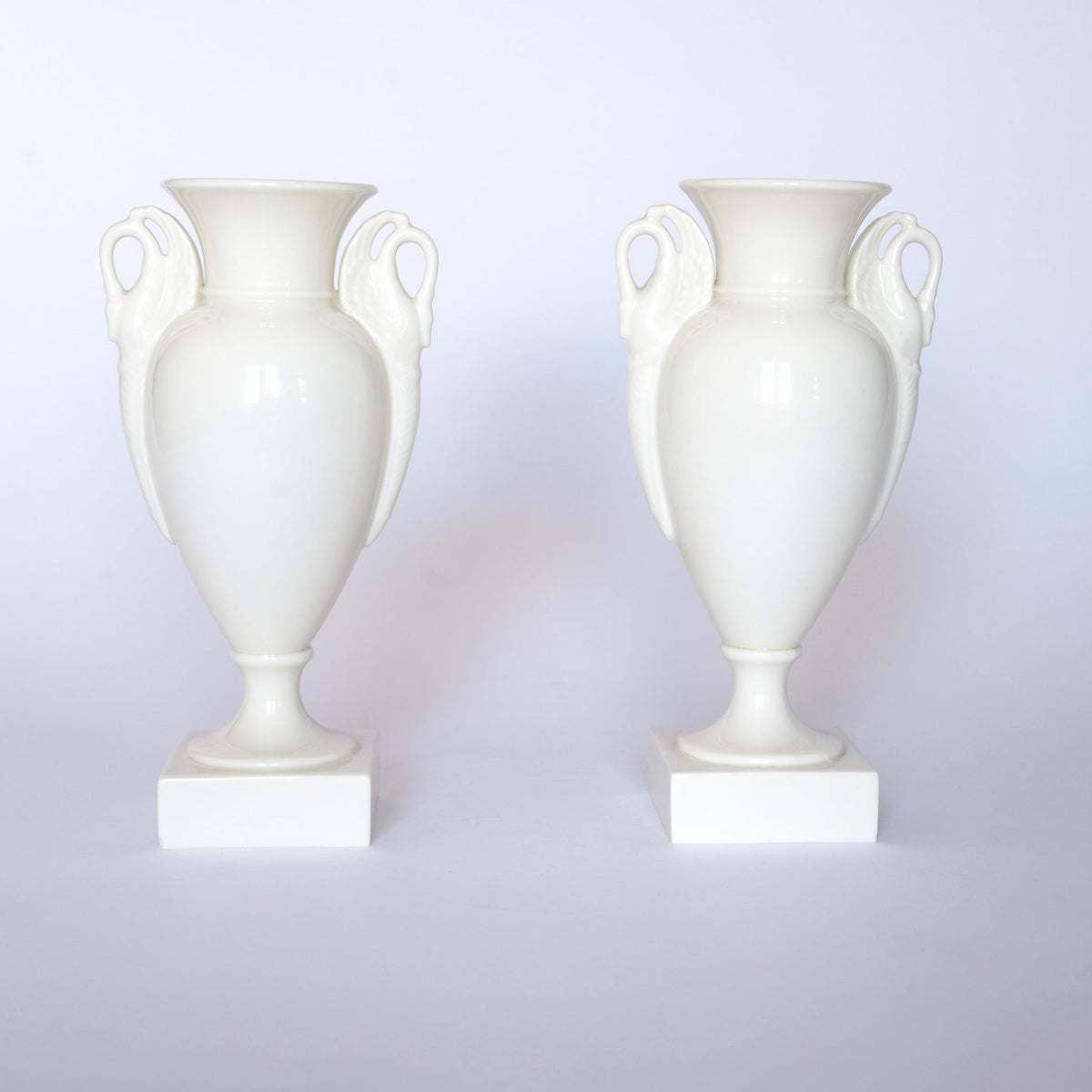 Pair of Vintage White Swan Handle Ceramic Urn Vases by Euro Trash, each featuring elegant swan handles and set on square bases against a plain white background.